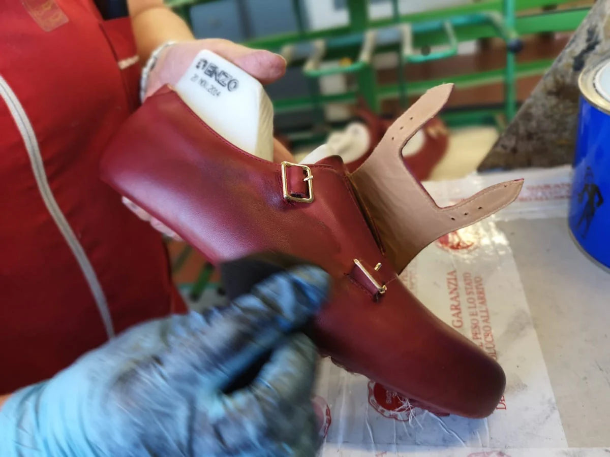 Red shoe with gold buckle held by a person wearing gloves, blurred background