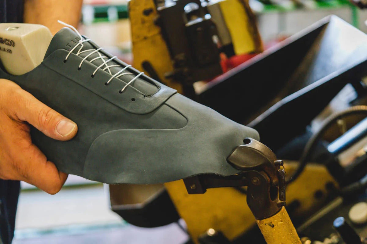 Person holding a black shoe with white laces in a workshop setting