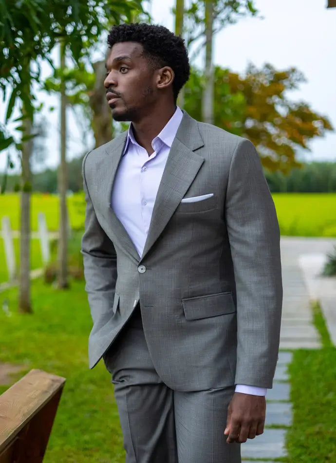Man in a sage suit standing outdoors with greenery in the background
