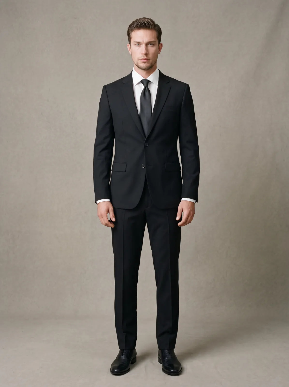 A man in a black suit, white shirt, dark tie and black leather shoes for a funeral