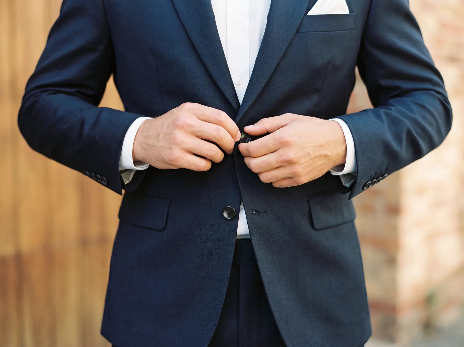 A man fastening the top button of a navy suit jacket with the bottom button left open