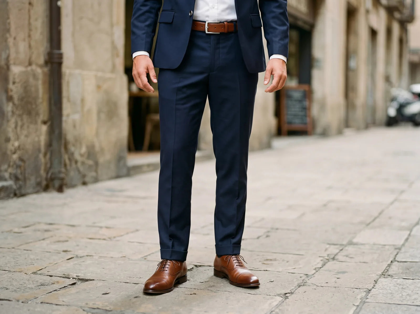 A man in a navy suit with a brown belt matching brown leather shoes