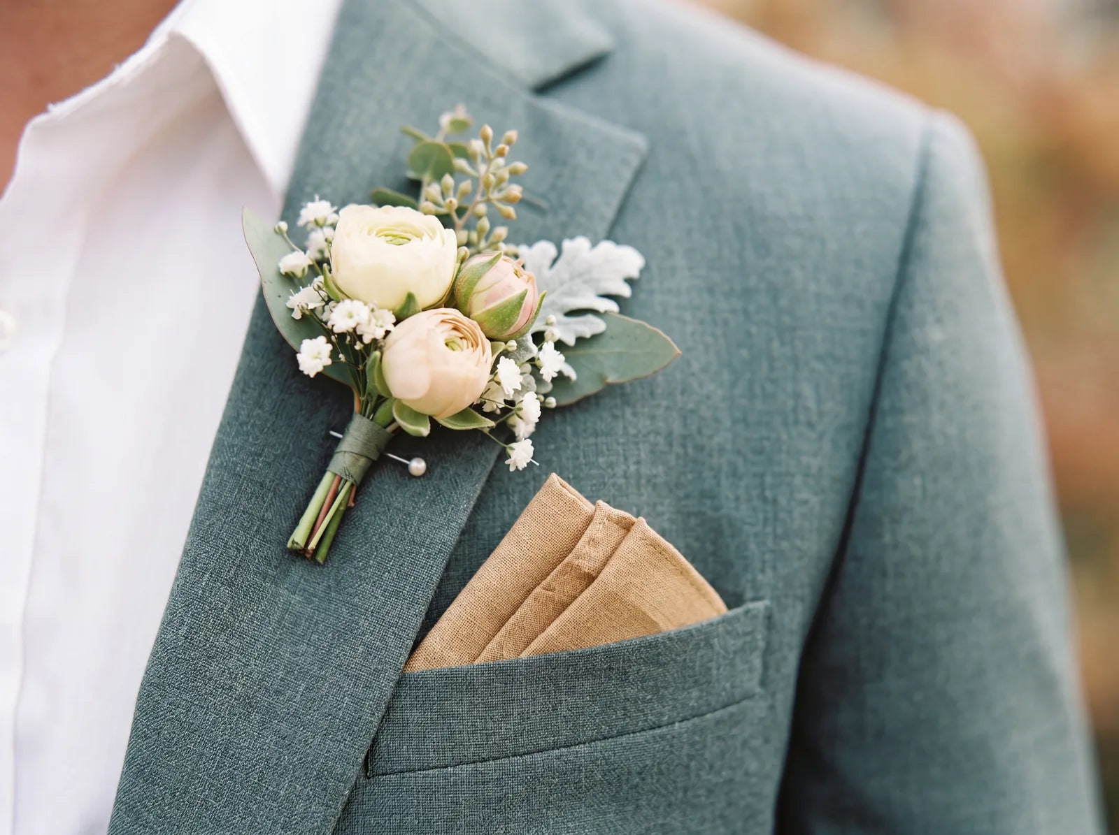 Close-up of a sage green suit lapel with a floral boutonniere and pocket square