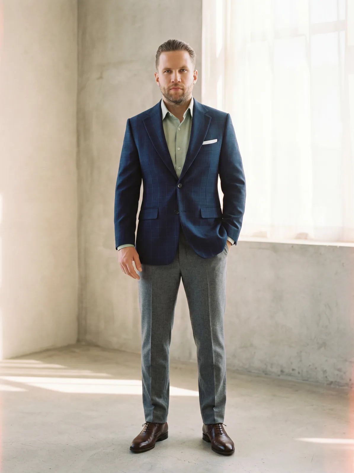 A man wearing a navy windowpane blazer with grey trousers and brown shoes