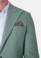 A close-up of a man wearing a sage green linen blazer over a white dress shirt, with a matching textured gray pocket square in the breast pocket124