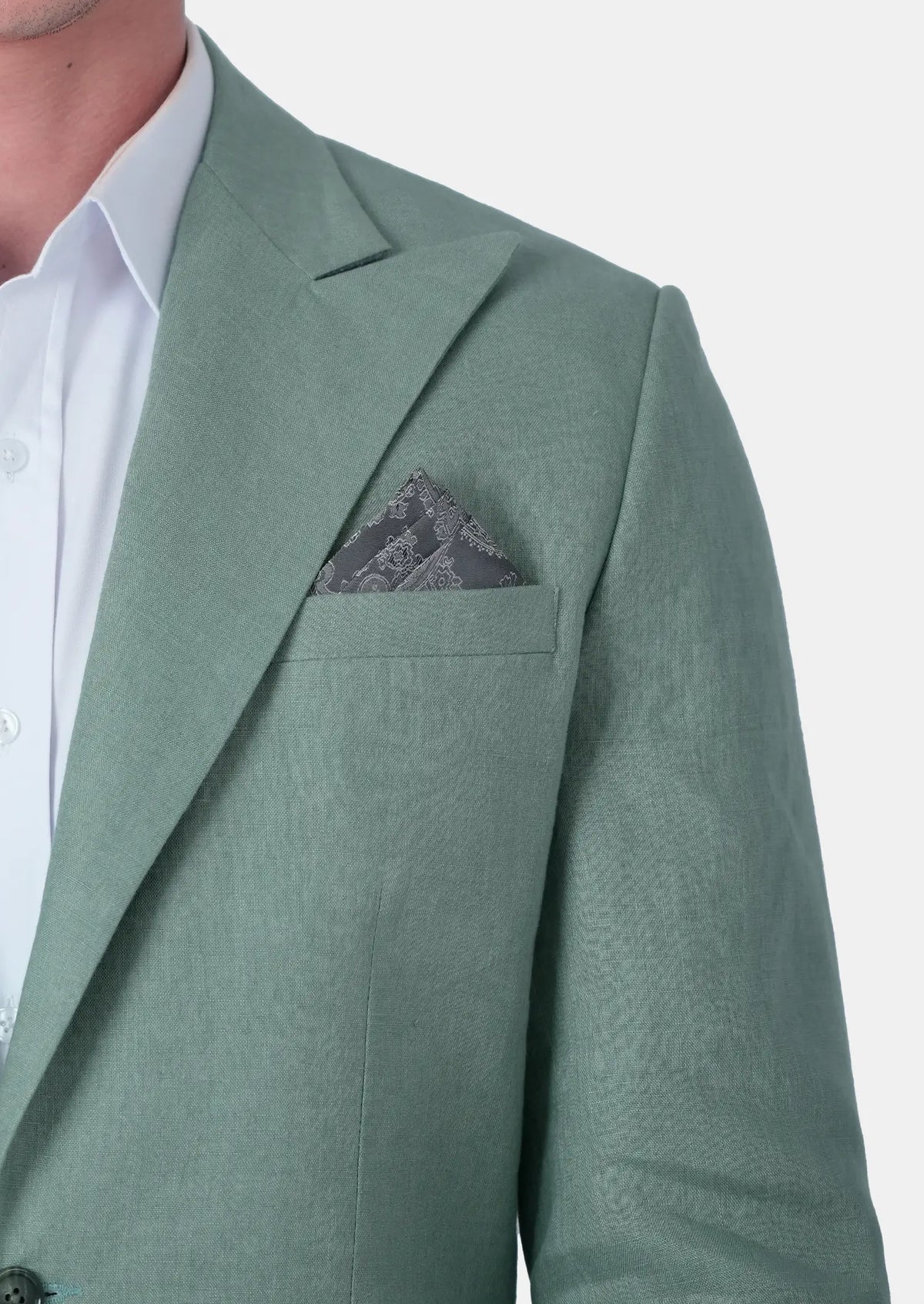 A close-up of a man wearing a sage green linen blazer over a white dress shirt, with a matching textured gray pocket square in the breast pocket743
