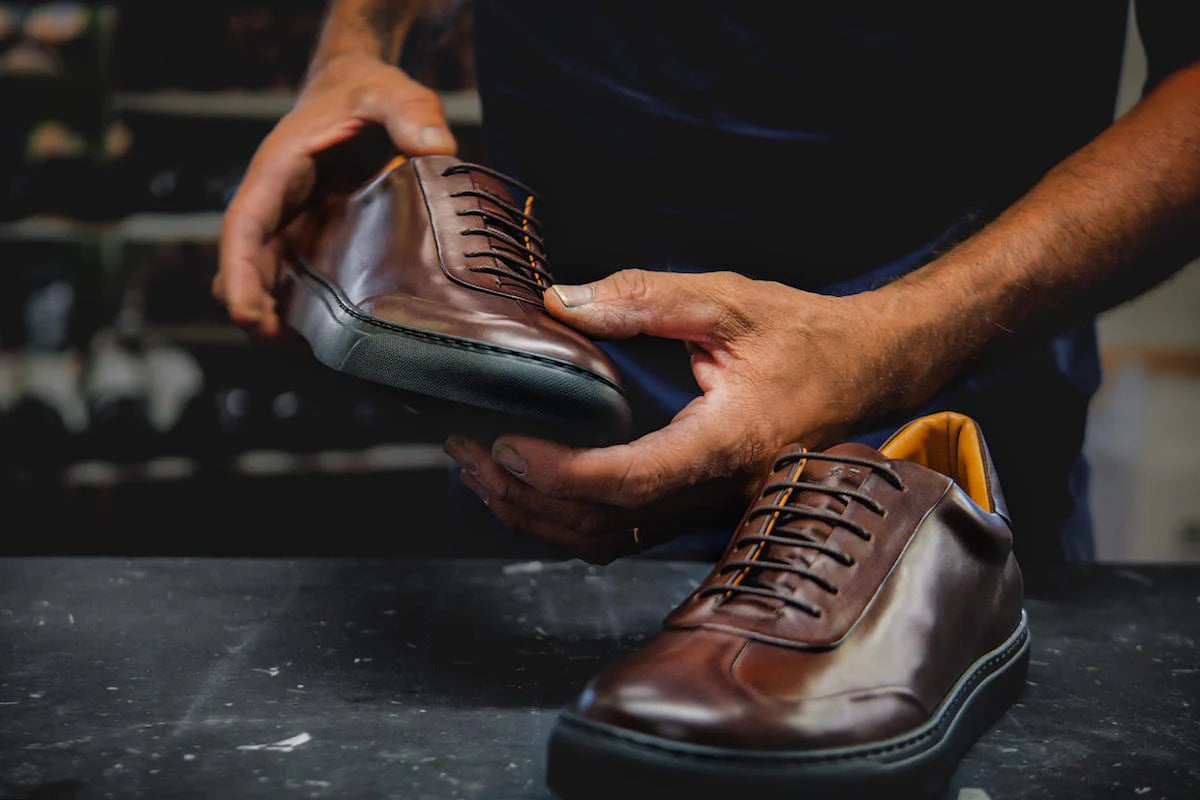 Person holding a brown leather shoe with visible laces on a dark surface.