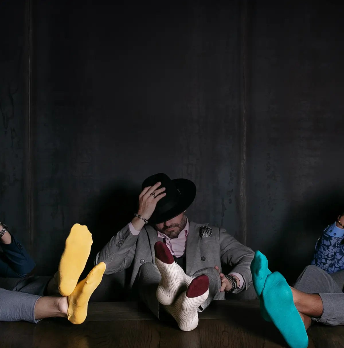 Three people sitting around a dark table with their feet on the table, wearing colorful shoes80