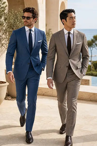 Two men walking outdoors in tailored suits. The man on the left wears a medium blue suit with a blue tie and white shirt.