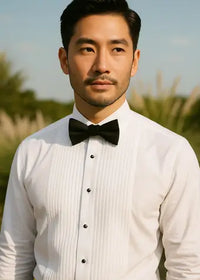 Man wearing a white tuxedo shirt with black bow tie and vest outdoors.