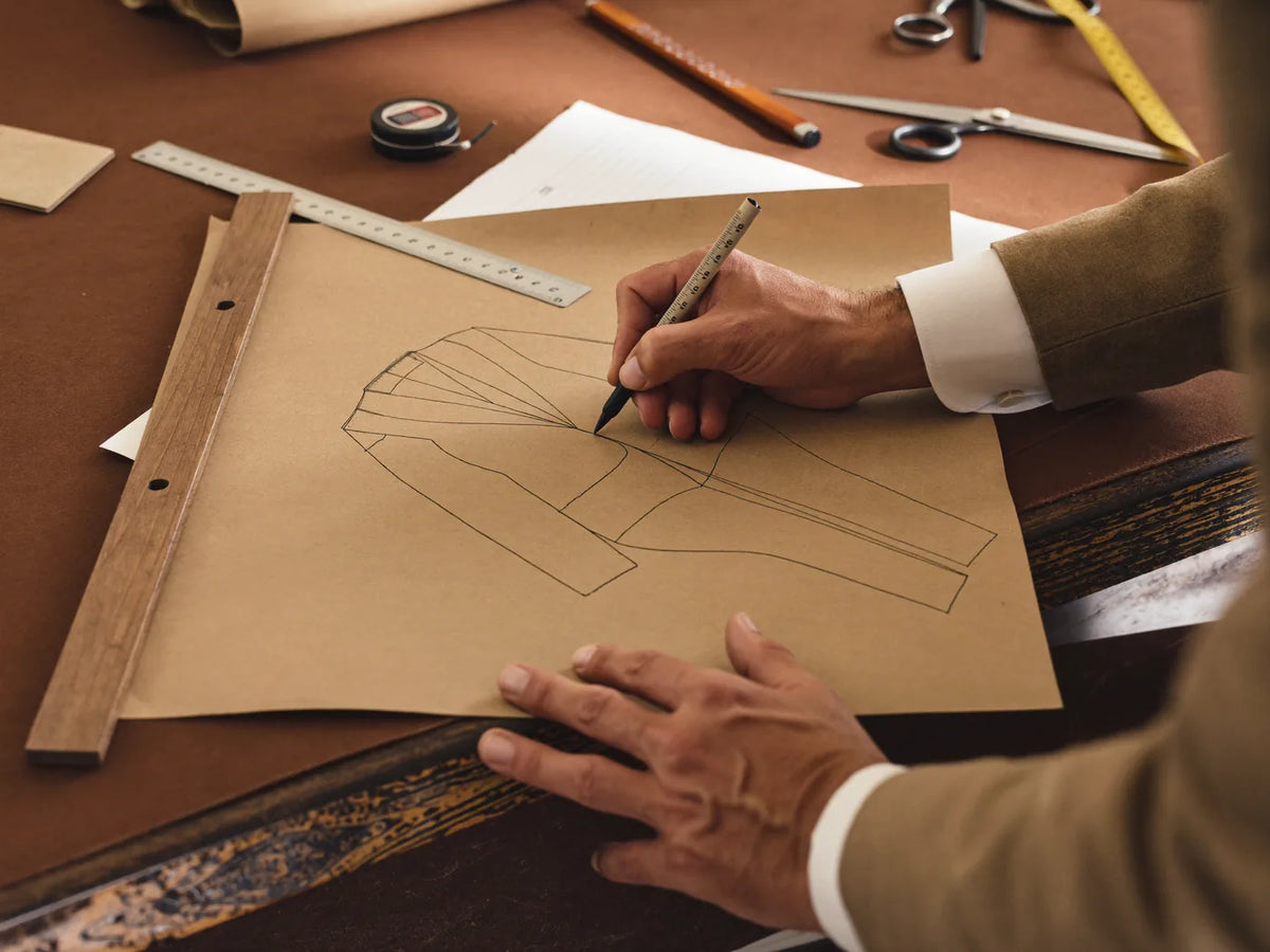 A tailor's hands drafting a bespoke suit pattern on kraft paper with a ruler and chalk