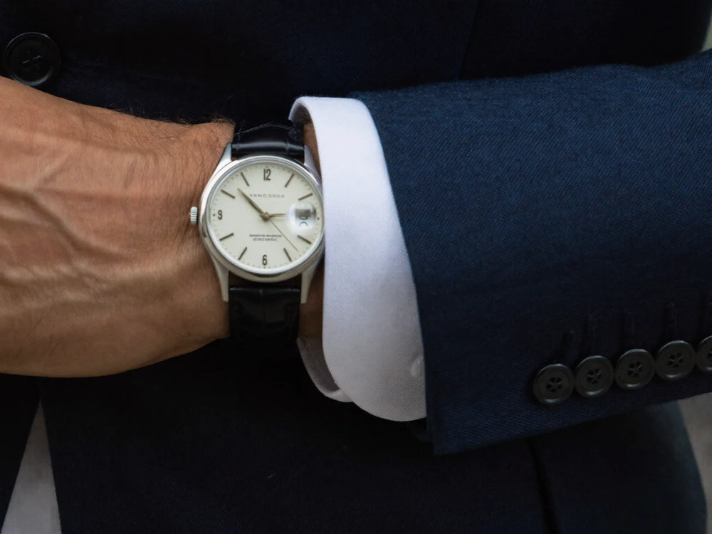 A classic analog wristwatch worn under a navy suit sleeve and white shirt cuff