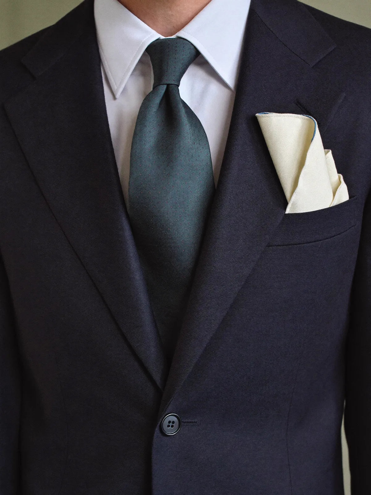 Tight detail of cocktail attire, navy lapel, white collar, muted teal silk tie, and ivory linen pocket square layered together