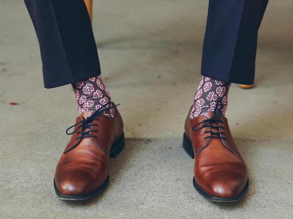 Brown leather oxford shoes worn with patterned dress socks and navy trousers