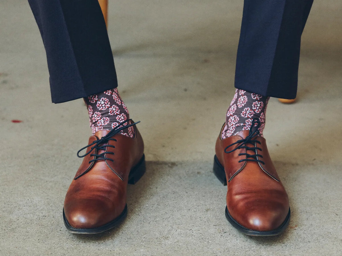 Brown leather oxford shoes worn with patterned dress socks and navy trousers