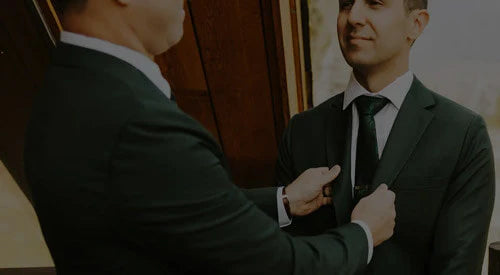 Two men in suits standing next to a red barn with mountains in the background