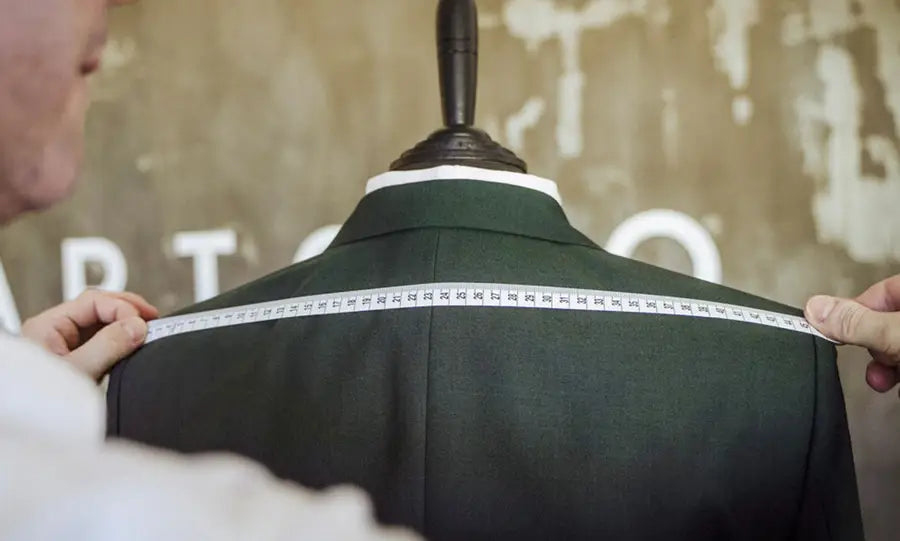 a man measuring the shoulder of a suit jacket on a mannequin bust