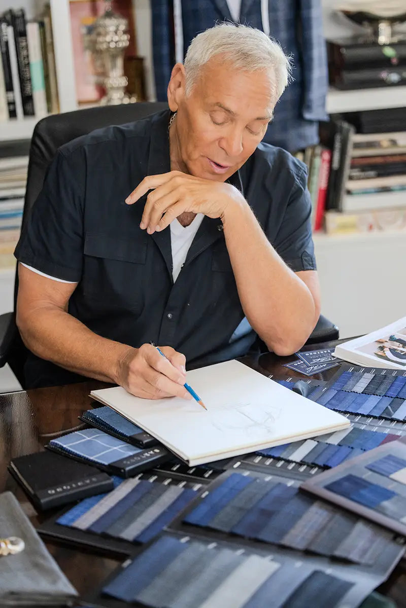 Neil Lane drafting suit designs at a table with fabric samples spread across.