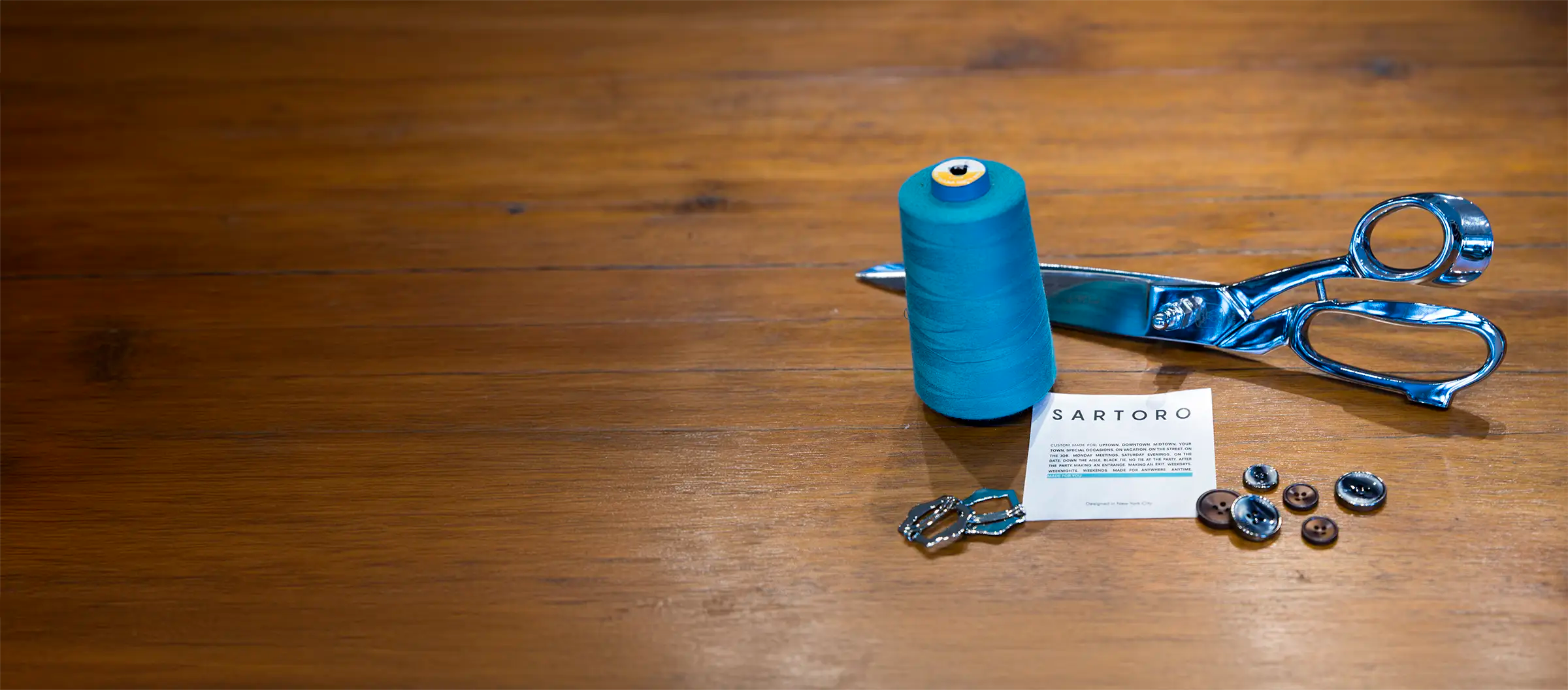 scissors, thread, a suit patch and buttons on a wood table