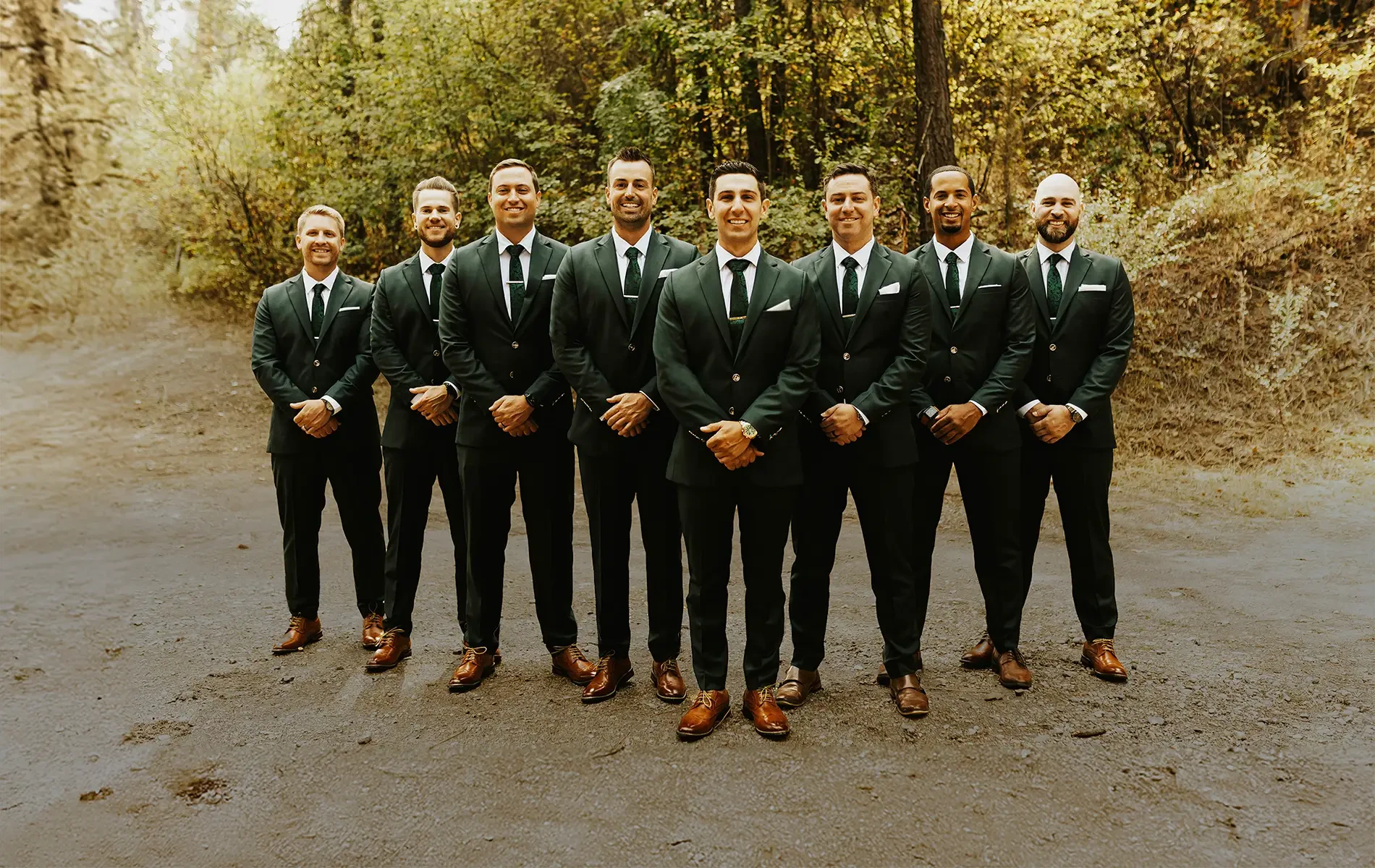 Group of men in suits standing in a line outdoors with trees in the background