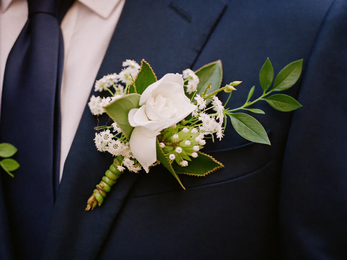 A white rose boutonniere on a navy suit lapel with a navy tie