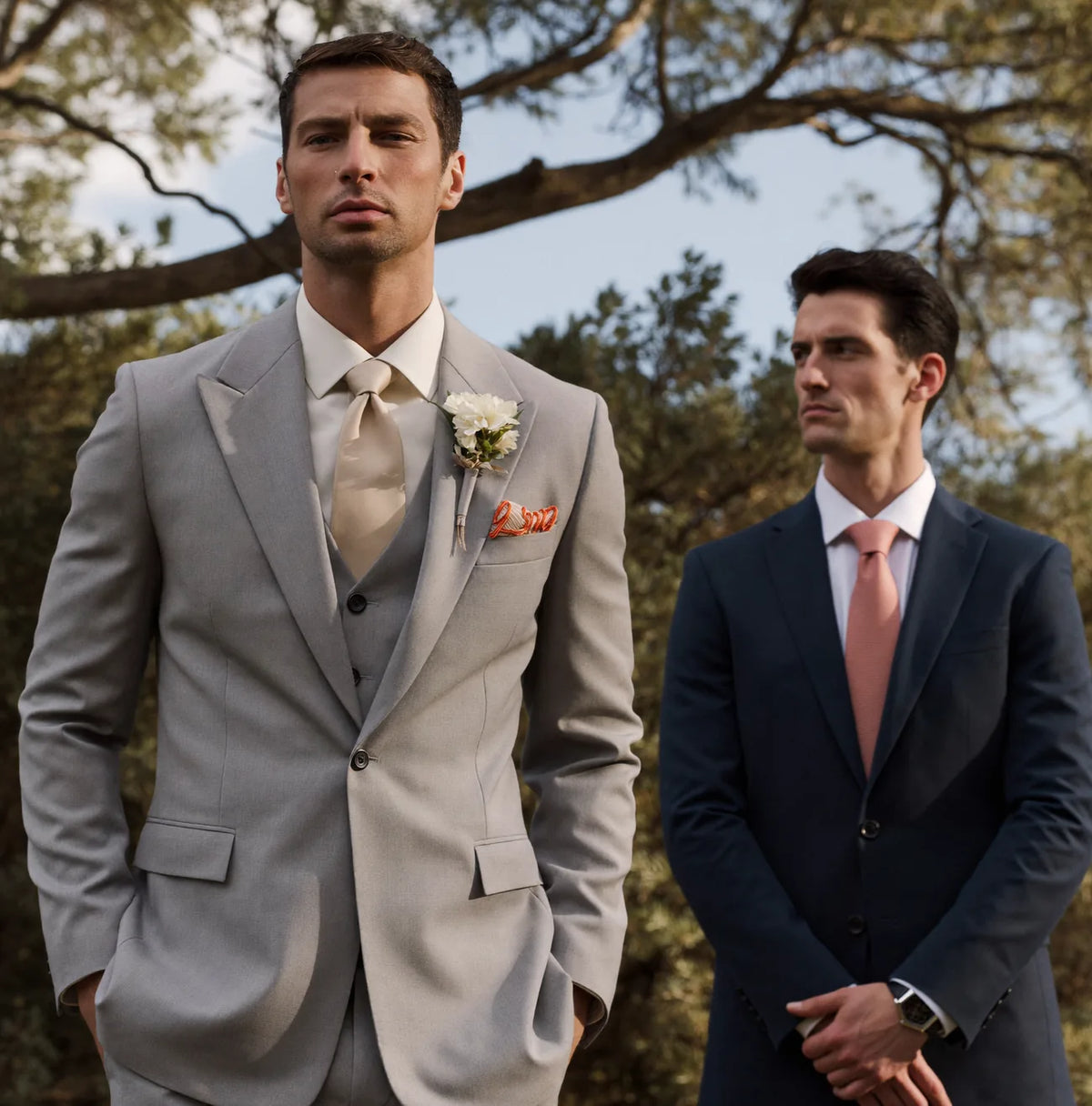 A groom in a light grey suit standing apart from a groomsman in navy