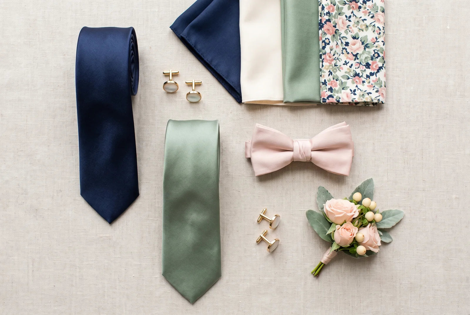 Wedding accessories flat-lay with ties, a bow tie, pocket squares, cufflinks, and a boutonniere