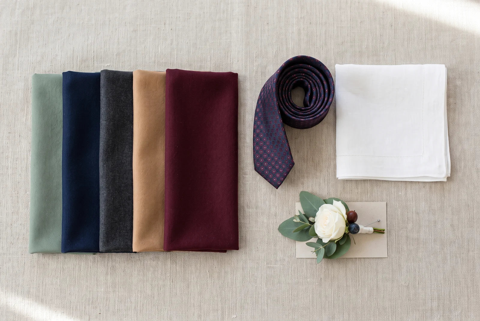 Wedding color palette swatches in sage green, navy, charcoal, tan, and burgundy with a tie and boutonniere