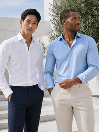 Two men standing outdoors wearing long-sleeve dress shirts, one in white and one in light blue, paired with dark trousers and light beige trousers respectively.