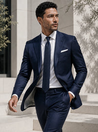 A man wearing a navy blue three-piece suit, white dress shirt, and matching navy tie, walking outdoors on stone steps.