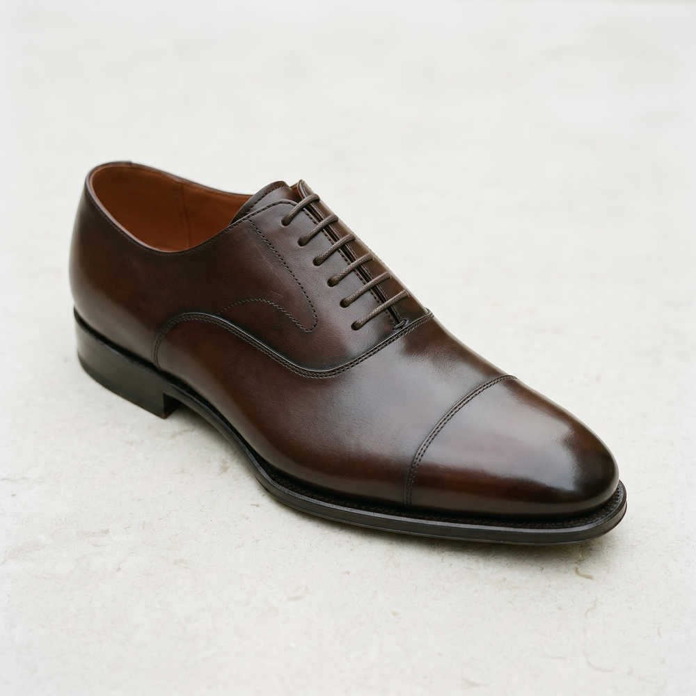 Dark brown cap-toe oxford shoe product shot showing closed lacing, clean toe shape, and slim leather sole