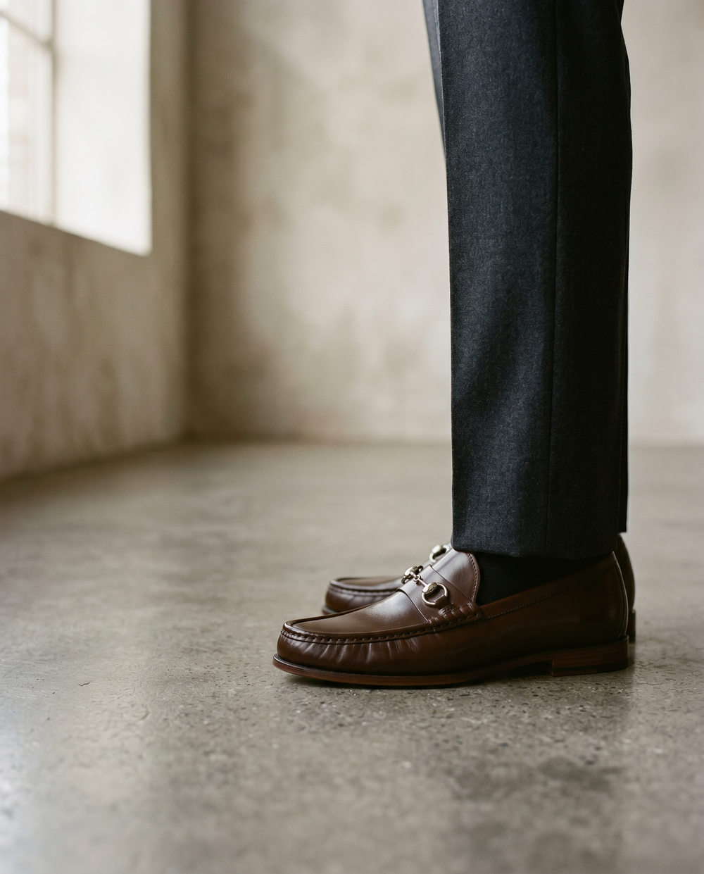 Dark brown horsebit loafer with polished metal bit detail, worn with tailored trousers