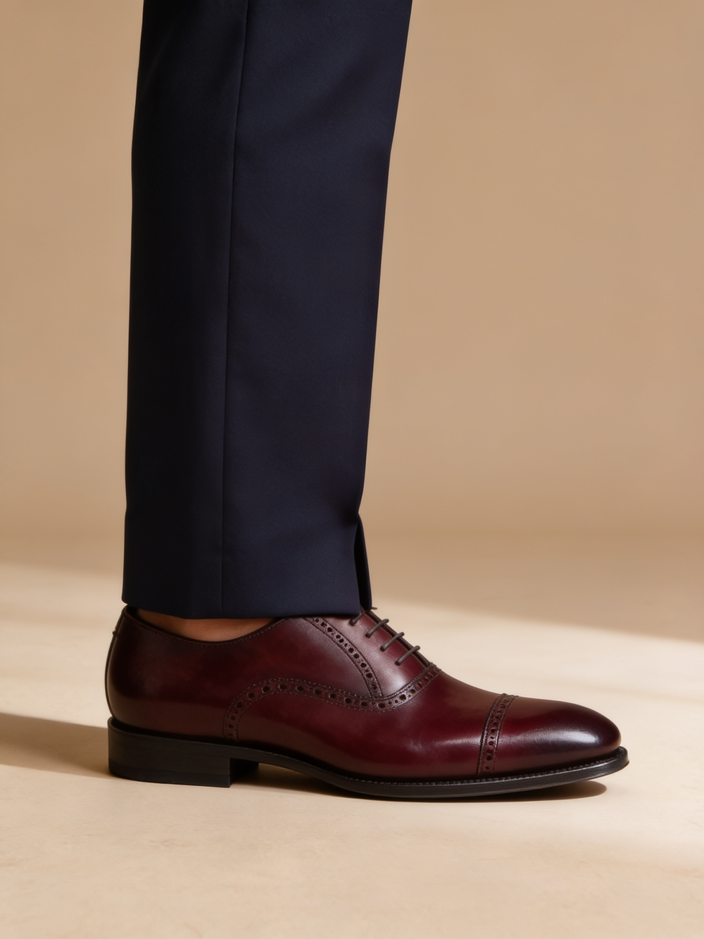 A deep oxblood brogue oxford, the warm reddish shade between brown and black, worn with a navy suit.