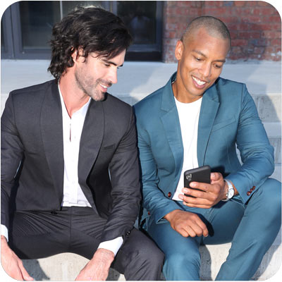 two models sitting using a phone, one in black suit, one in blue suit