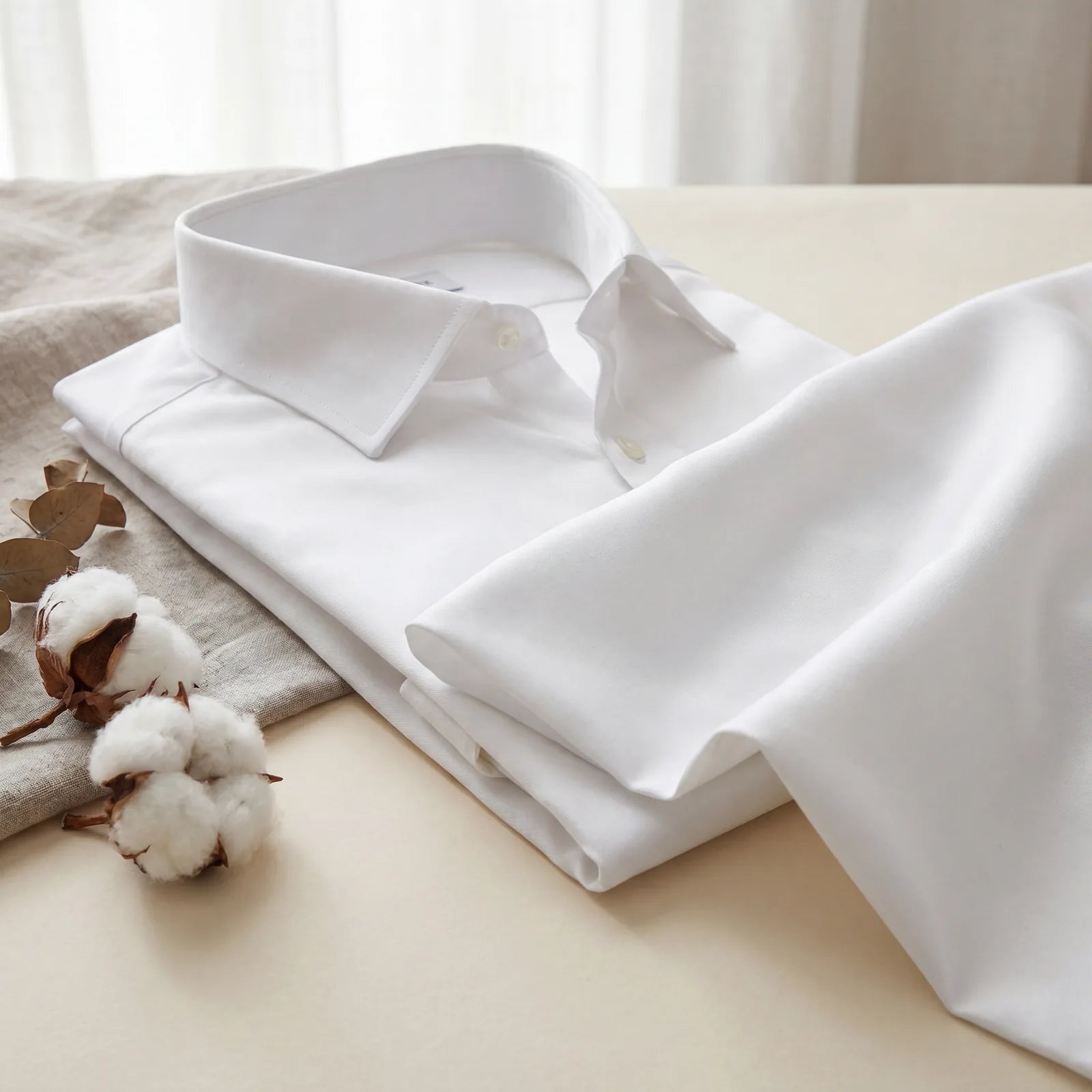 A folded white long-staple cotton dress shirt beside raw cotton bolls