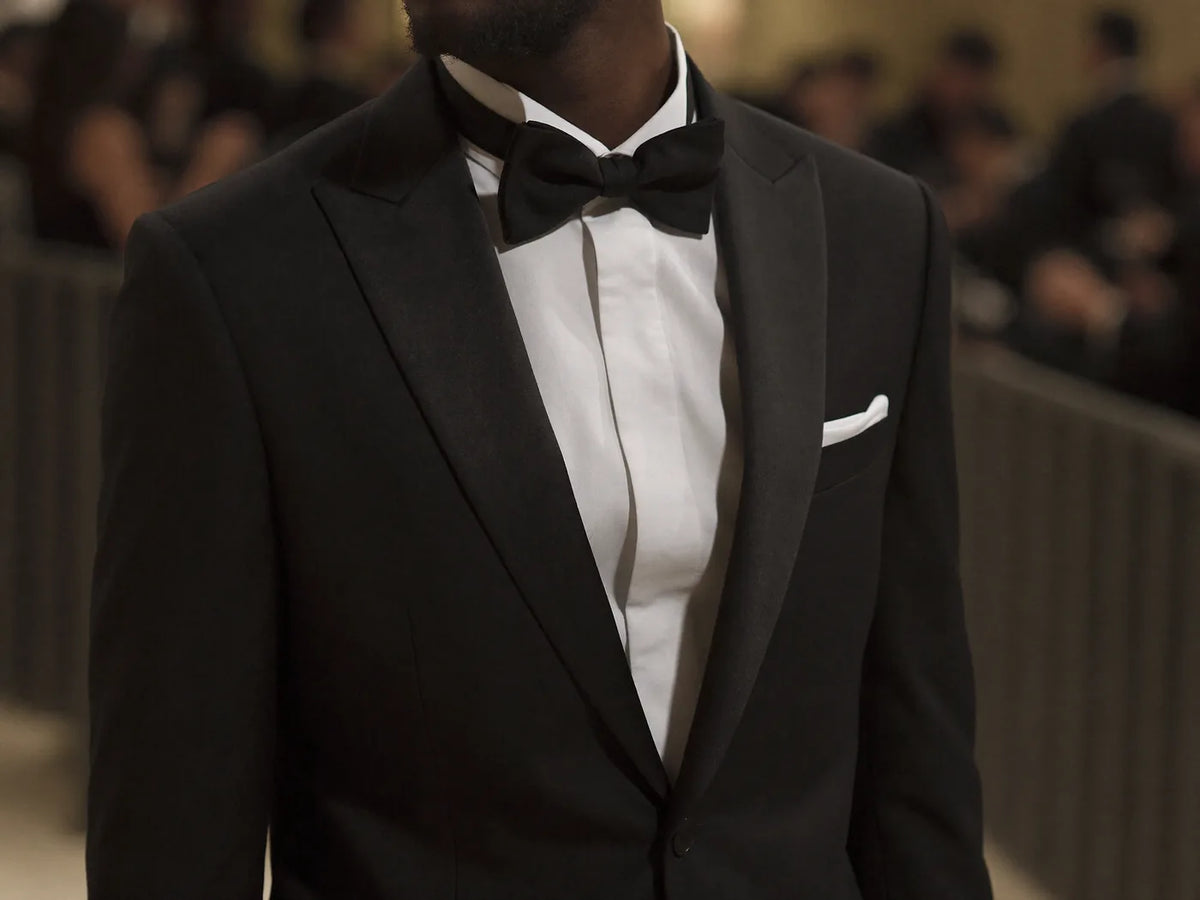 A man wearing a black tuxedo with a bow tie and pocket square at a formal evening event