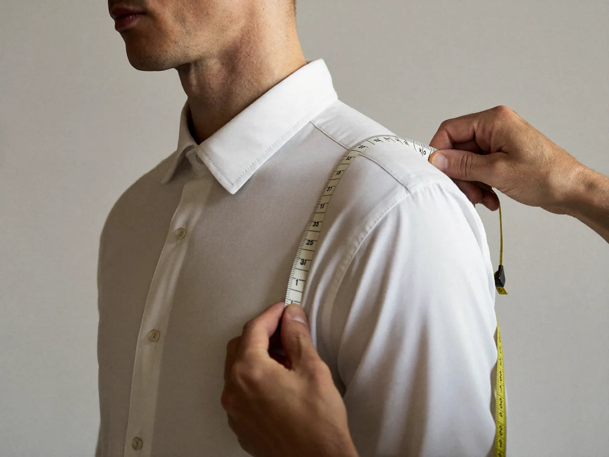 Measuring a man's shoulder with a soft tape measure over a white shirt