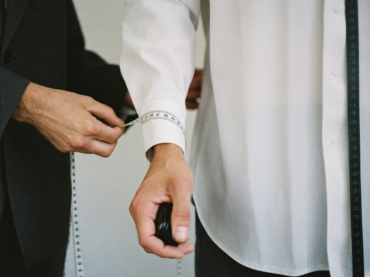 Measuring a man's sleeve length at the wrist with a soft tape measure