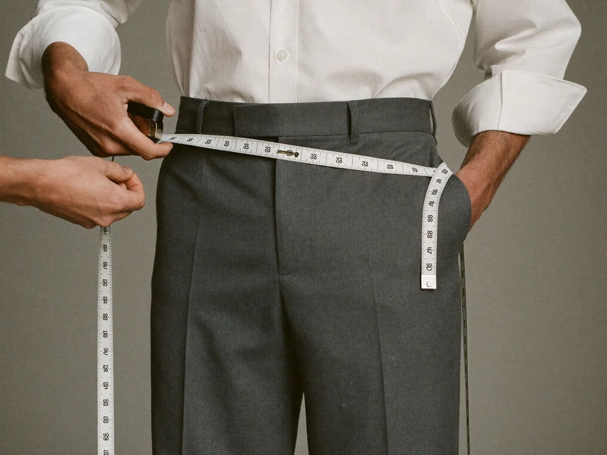 A tailor measuring a man's waist with a soft tape measure over trousers
