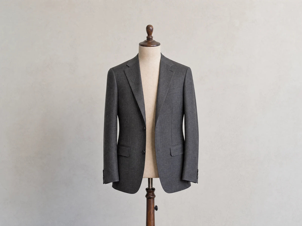 Charcoal men's suit jacket on a tailor's form, introducing the parts of jacket anatomy
