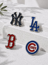 Four sports team enamel pins including New York Yankees, Los Angeles Dodgers, Boston Red Sox, and Chicago Cubs, arranged on a light gray stone block.