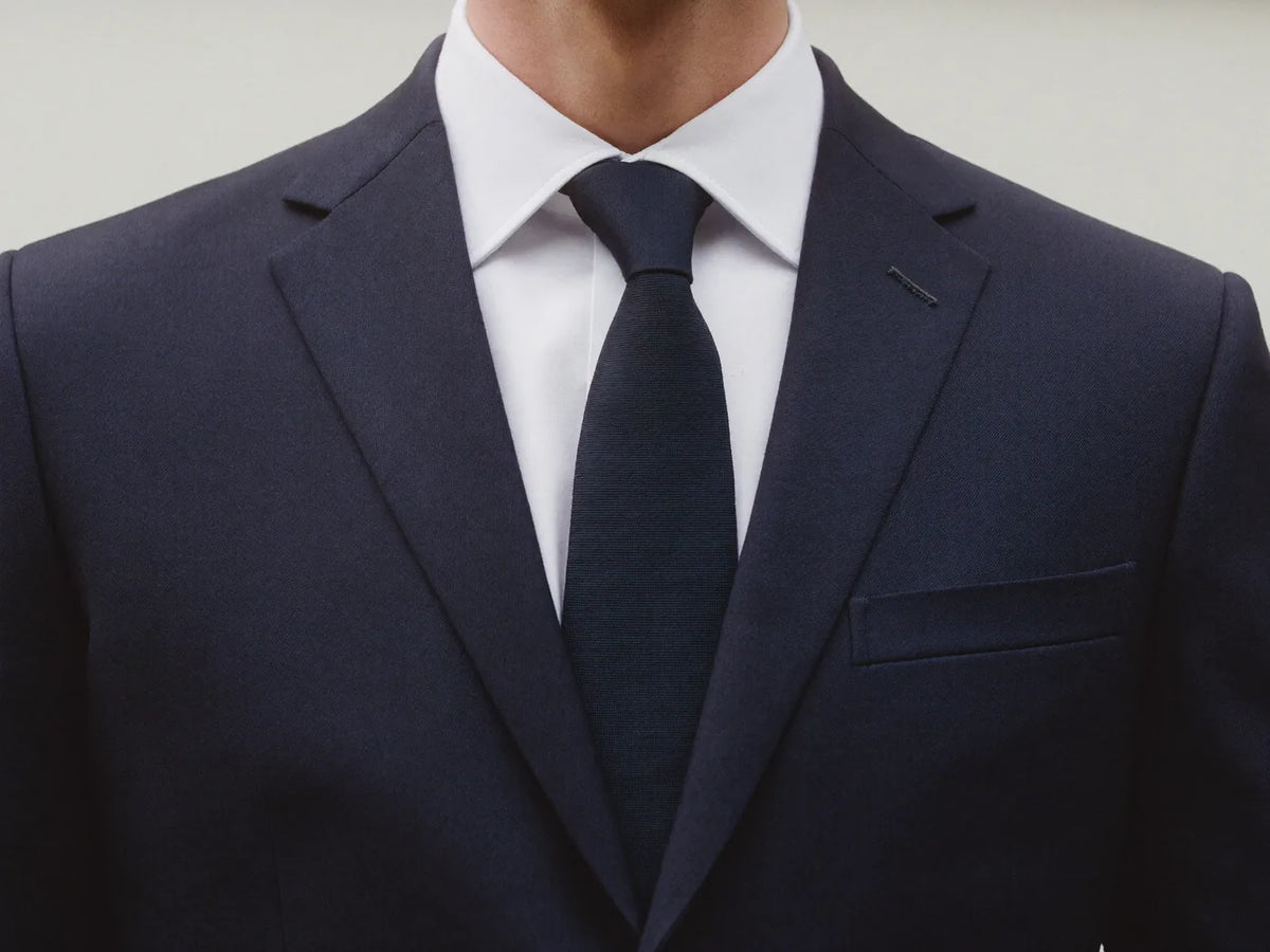 A man wearing a navy suit dressed up with a white shirt and navy tie