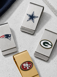 Four stainless steel money clip money clip holders with NFL team logos, including Dallas Cowboys, New England Patriots, Green Bay Packers, and San Francisco 49ers, arranged on a light gray textured surface.