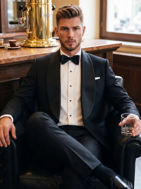 Man in a black tuxedo sitting in a bar holding a glass.
