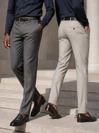 Two men wearing slim-fit dress pants, one in charcoal gray and the other in light beige, paired with navy shirts and brown loafers, walking down stone steps.