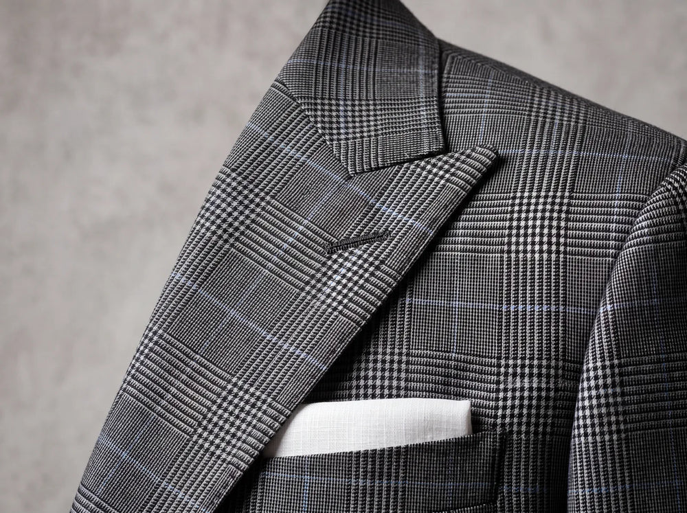 Close-up of a wide peak lapel on a charcoal Prince of Wales check suit jacket with a white pocket square