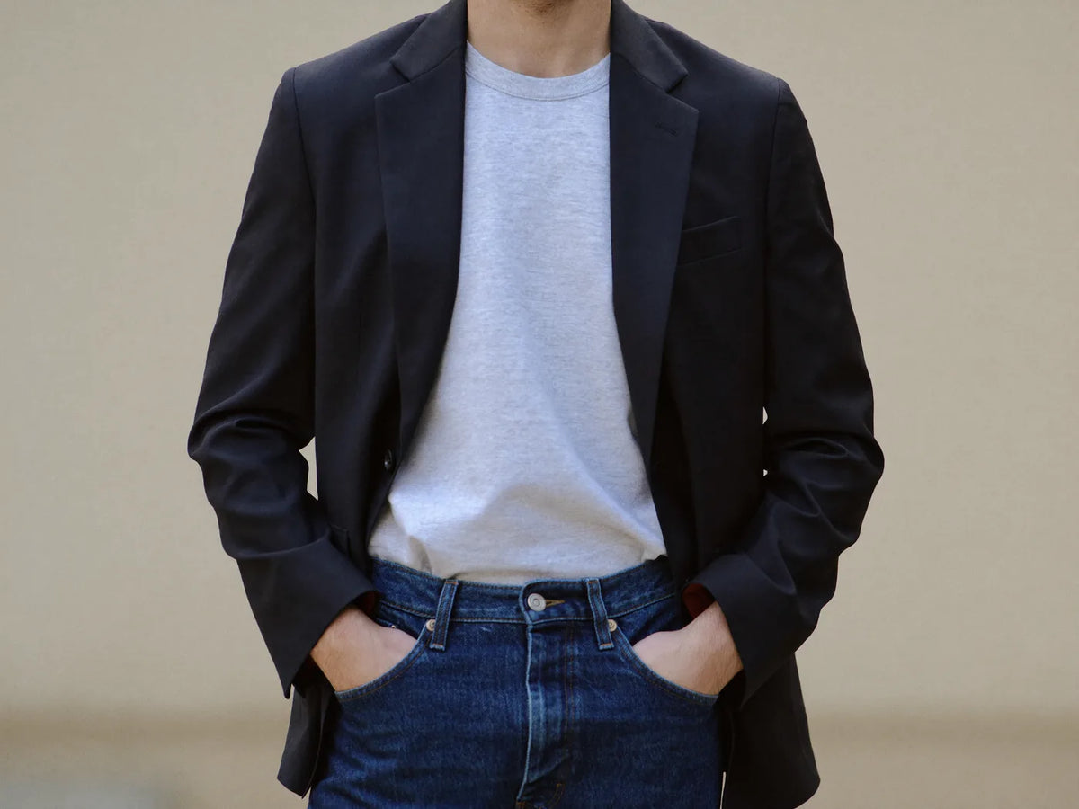 A man wearing a navy suit blazer with a grey t-shirt and dark jeans