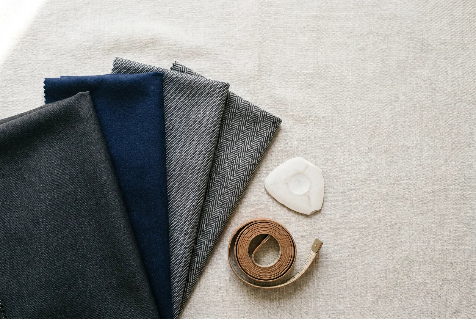 Suiting fabric swatches in wool, flannel, sharkskin, and a wool blend with a tailor's tape and chalk