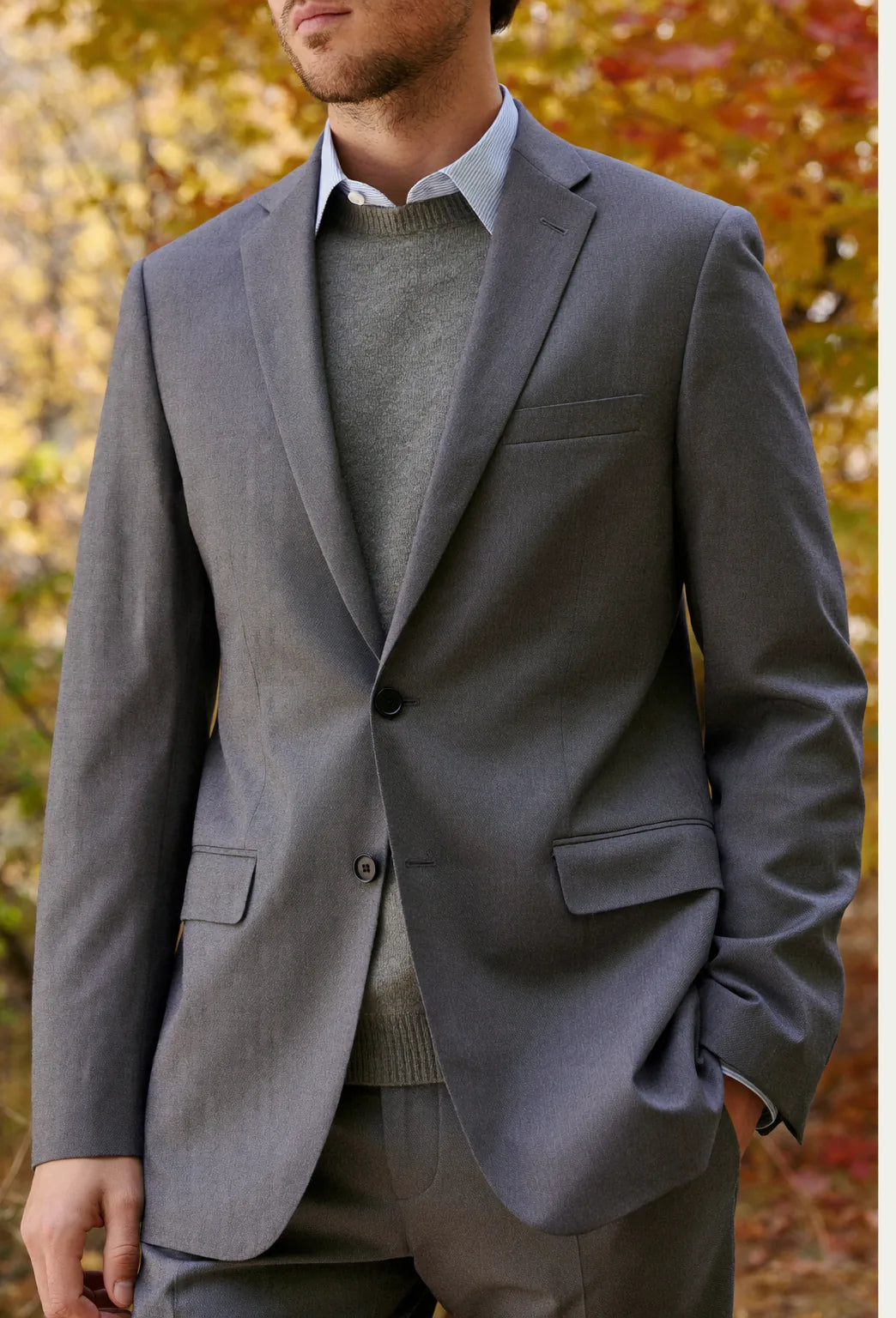 A man wearing a grey suit with a knit sweater layered over a shirt for autumn