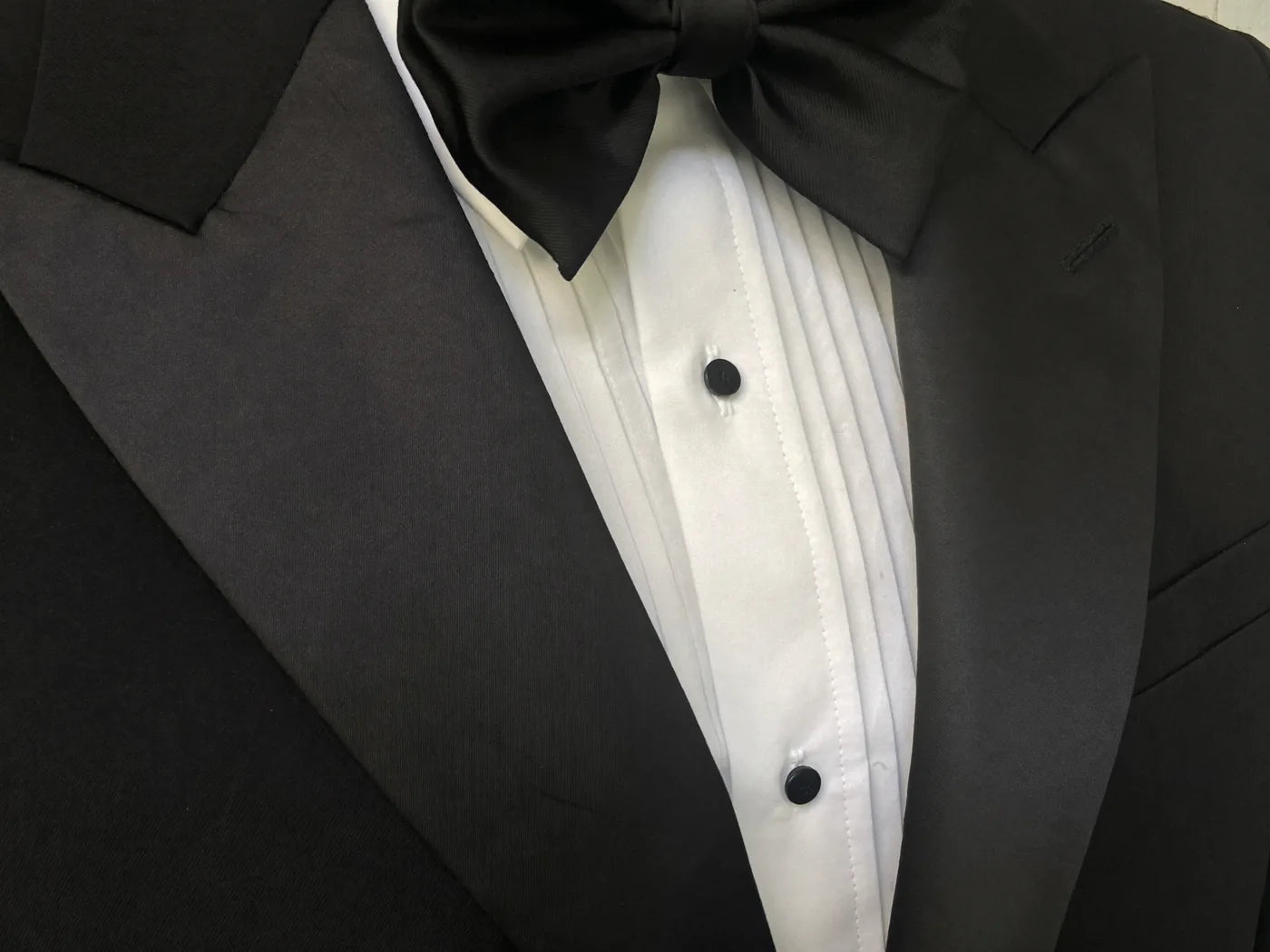 Close-up of a black tuxedo's satin lapel, black bow tie and studded white dress shirt